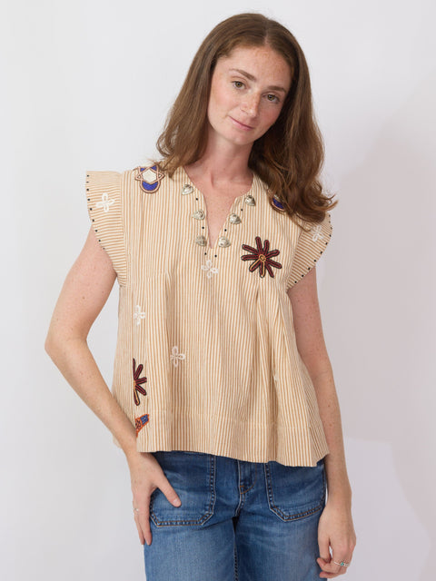 Woman wearing a beige sleeveless top with floral patterns and blue jeans on a white background
