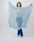 Light mid blue cashmere scarf held open showing lightweight, soft texture and large square shape.