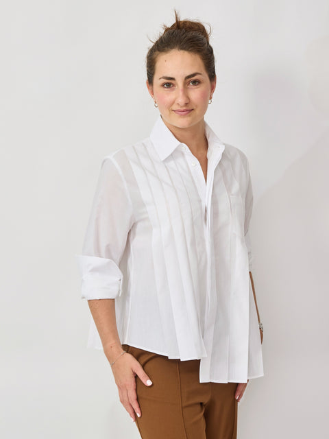 Woman wearing a white blouse and brown pants against a plain background