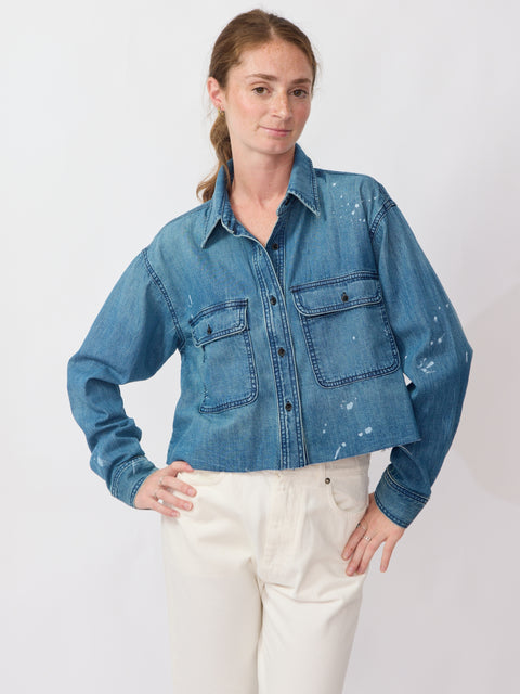 Woman wearing a blue denim jacket with white paint splashes on a plain background