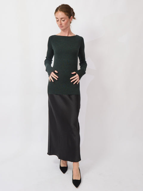 Woman wearing a dark green long-sleeve top and black skirt on a white background