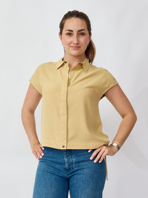 Woman wearing a beige short-sleeve shirt and blue jeans against a white background