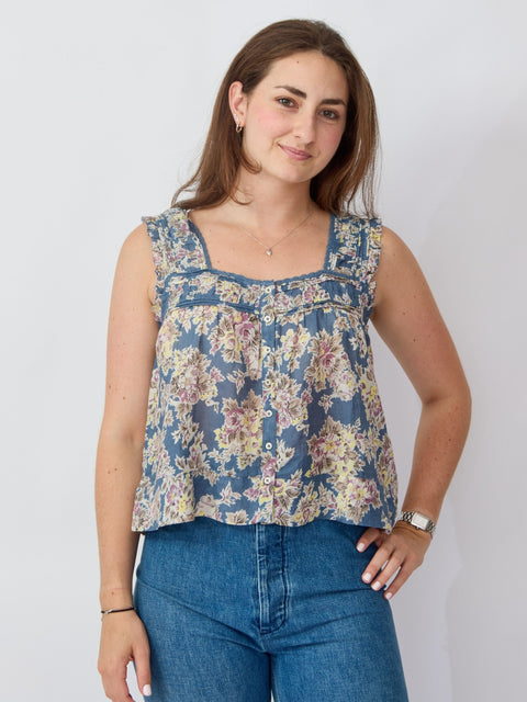 Woman wearing a floral sleeveless top and blue jeans against a plain background