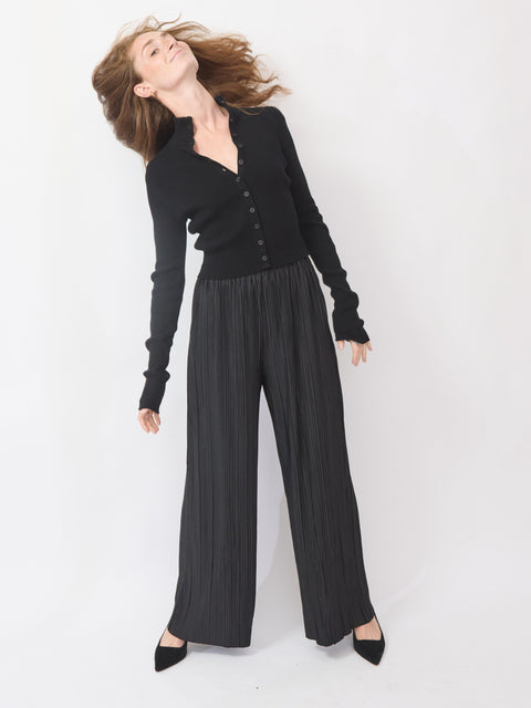 Woman wearing a black cardigan and pleated black pants on a white background