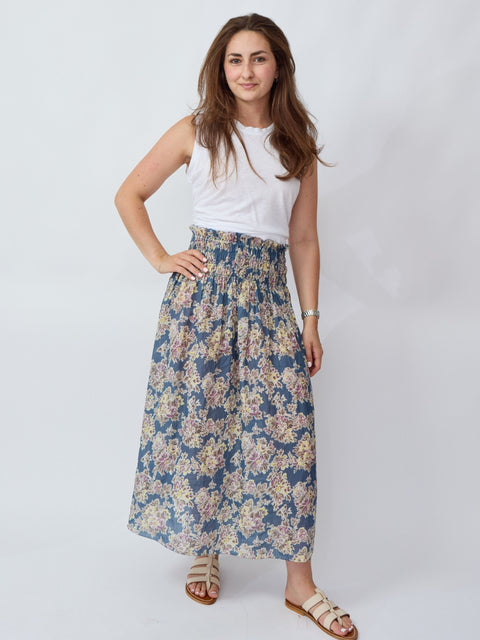 Woman wearing a white top and floral skirt on a plain background