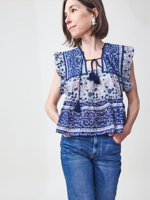 A woman wearing a navy floral sleeveless top with tassel ties and a wide ruffle hem, paired with blue jeans.