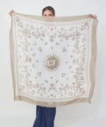 Taupe and white square bandana with floral patterns and central circular logo.