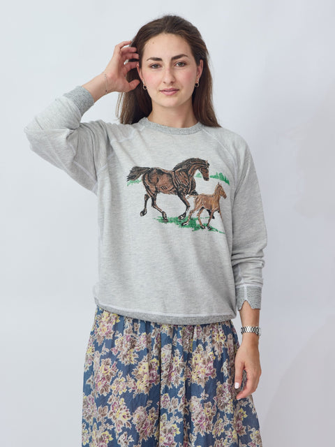 Woman wearing a gray sweatshirt with horse design on a plain background