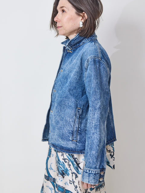 Woman wearing a blue denim jacket over a patterned dress on a plain background