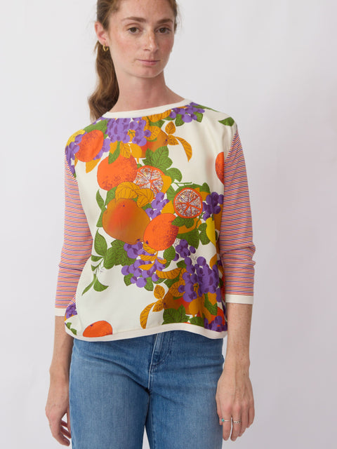 Woman wearing a colorful fruit-themed top with a plain background