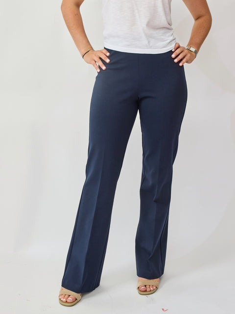 Person wearing navy blue pants and a white top on a plain background