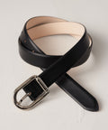Black leather belt with silver rectangular buckle and rounded tip on beige background.