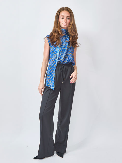Woman wearing a blue patterned top and black pants on a white background