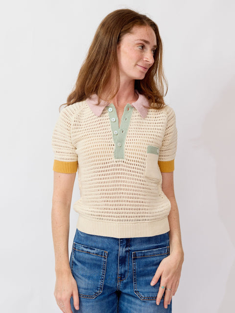 Woman wearing a light-colored knit sweater with yellow accents and blue jeans on a plain background