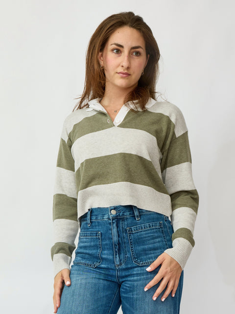 Woman wearing a green and white striped sweater with blue jeans on a plain background