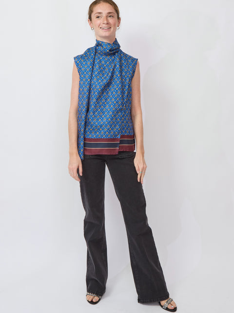 Woman wearing a blue patterned sleeveless top and black pants on a white background