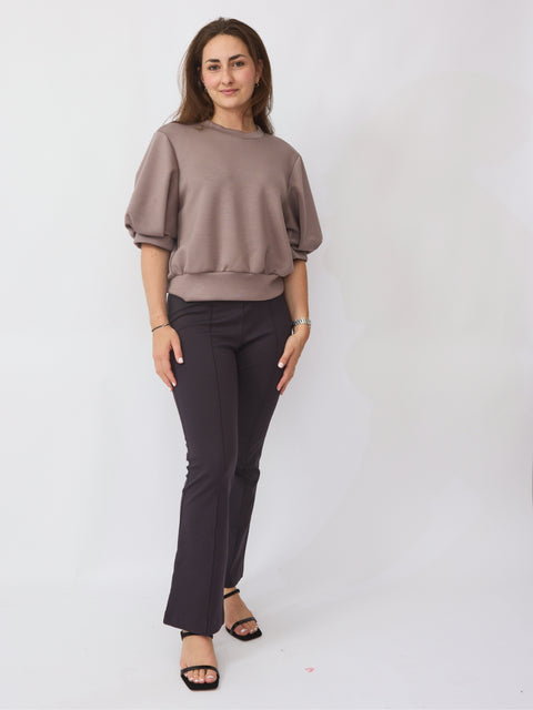 Woman wearing a brown top and black pants on a white background