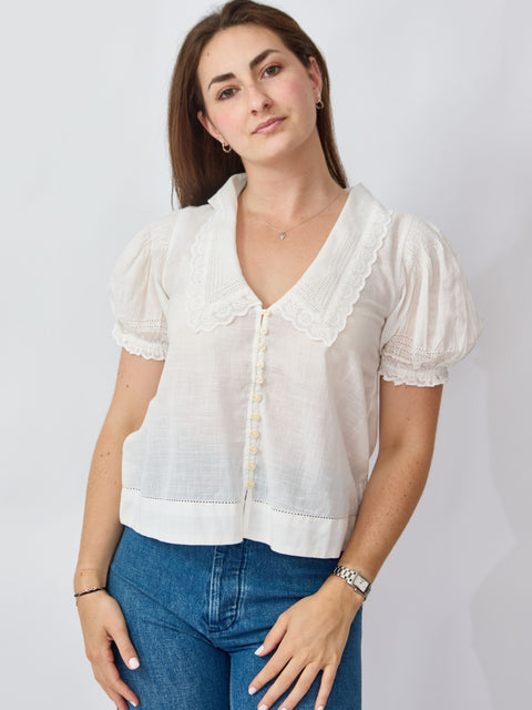 Woman wearing a white blouse with short sleeves and blue jeans on a plain background