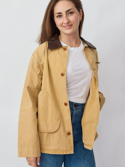 Woman wearing a beige jacket over a white shirt and blue jeans on a plain background