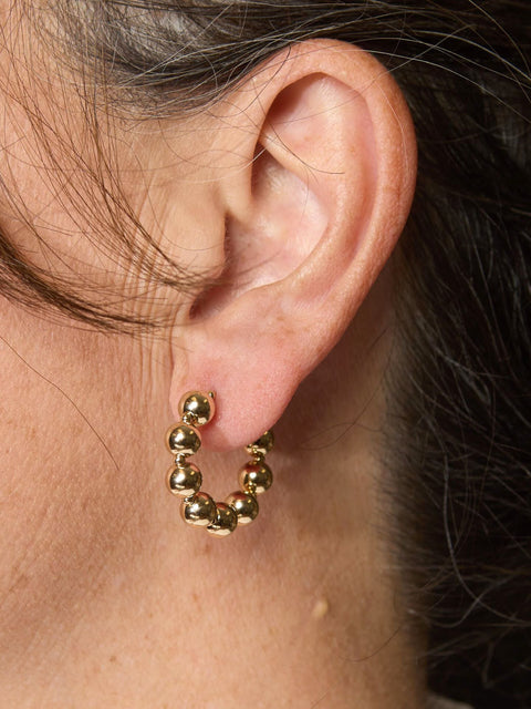 Woman wears small gold hoops with 14K gold-filled beads.