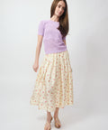 Ecru midi skirt with small floral print, paired with lilac short-sleeve top and nude sandals.