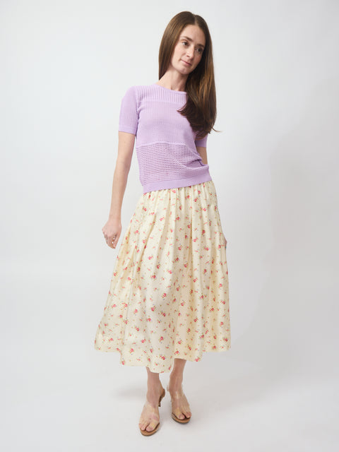 Ecru midi skirt with small floral print, paired with lilac short-sleeve top and nude sandals.