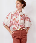 Woman wearing a floral blouse and red pants on a white background