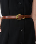 Mahogany leather belt with gold rectangular buckle worn over black buttoned garment.