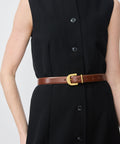 Mahogany leather belt with gold buckle on black sleeveless buttoned dress.