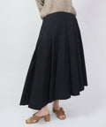 Black midi skirt with asymmetrical hem and flowing pleats, paired with tan block-heel sandals.