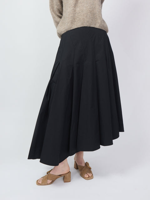 Black midi skirt with asymmetrical hem and flowing pleats, paired with tan block-heel sandals.