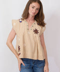 Woman wearing a beige sleeveless top with floral patterns and blue jeans on a white background