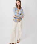 Long-sleeve camel and blue check button-up shirt with a relaxed fit worn with cream wide-leg pants and black sandals.
