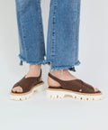 Chestnut brown leather sandals with crisscross straps and white chunky sole, worn with frayed hem blue jeans.