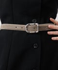 Grey suede belt with a shiny silver oval buckle worn over a black buttoned dress.