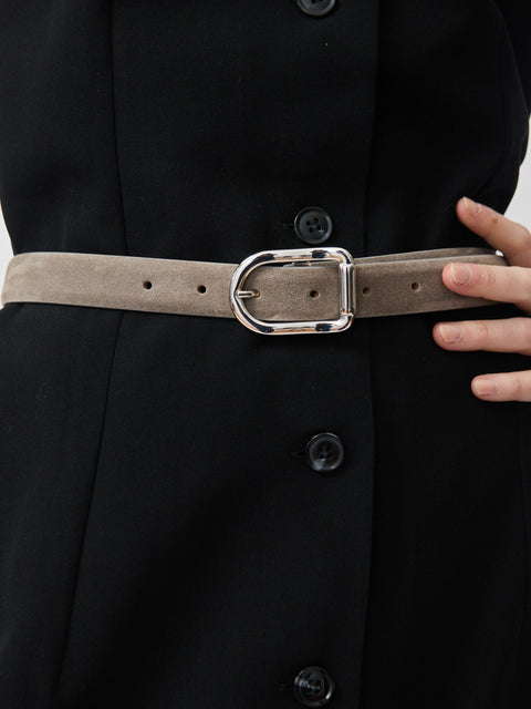 Grey suede belt with a shiny silver oval buckle worn over a black buttoned dress.