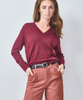 Woman wearing a burgundy sweater and pink pants against a light gray background