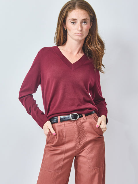 Woman wearing a burgundy sweater and pink pants against a light gray background