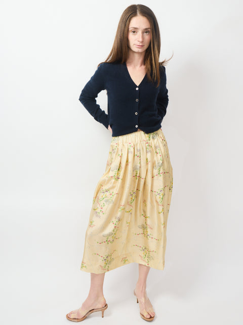 Yellow midi skirt with green floral embroidery paired with a black button-up cardigan and beige heeled mules.