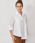 Woman wearing a white blouse and brown pants against a plain background