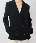 Black double-breasted blazer with wide lapels, structured shoulders, and side pockets.