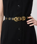 Black leather belt with gold double-ring buckle and gold rivet accents worn over a black dress.