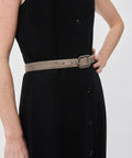 Grey suede belt with silver rounded buckle worn over black dress.