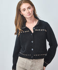 Woman wearing a black cardigan with decorative buttons on a light gray background