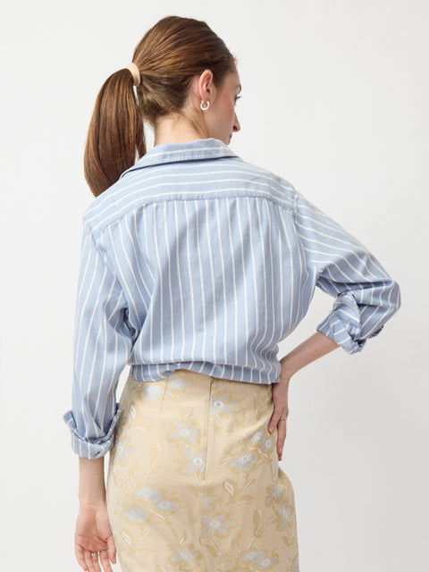 Blue and white vertically striped button-up shirt with long sleeves and a collar, styled tucked in.