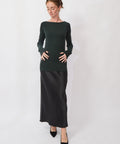 Woman wearing a dark green long-sleeve top and black skirt on a white background