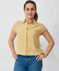Woman wearing a beige short-sleeve shirt and blue jeans against a white background