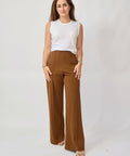 Woman wearing brown wide-leg pants and a white sleeveless top on a plain background
