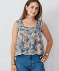 Woman wearing a floral sleeveless top and blue jeans against a plain background