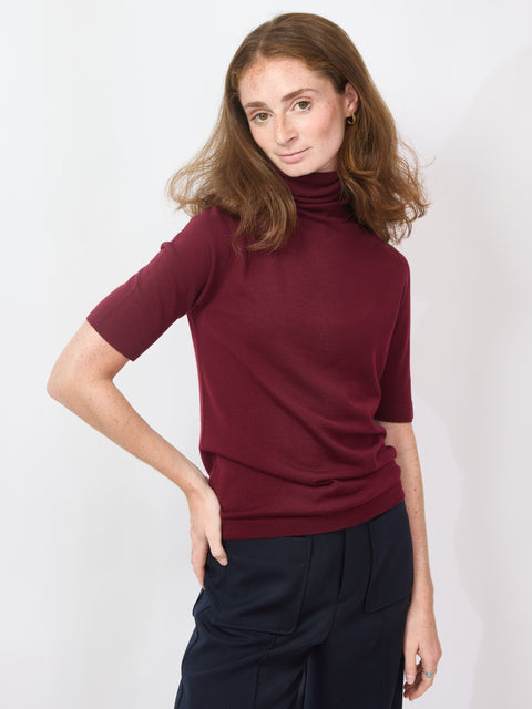 Woman wearing a burgundy turtleneck sweater and dark pants against a white background